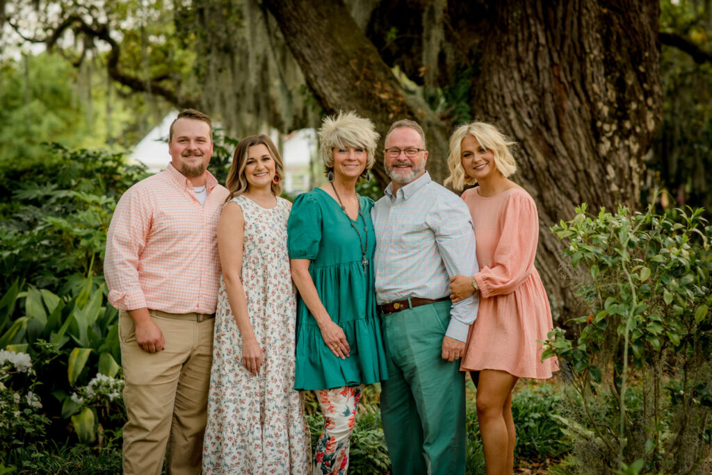 Pastors Tom and Terri Wallace posing with their family in a bright green forest.